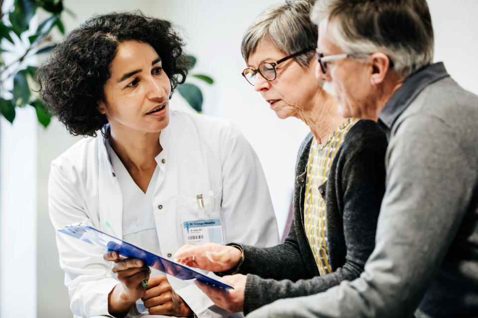 Clinician giving some test results to two elderly patients in hospital.