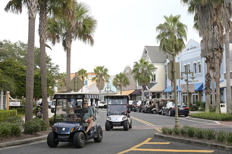 FILE - Residents drive golf carts through Market Square at Lake Sumter Landing in The Villages, Florida, on August 12, 2021.  Sumter County, Florida, home of The Villages, a booming retirement community, had the highest median age at 68.5 years.  Utah County, home to Provo, Utah, had the lowest score at 25.9.  (AP Photo/Phelan M. Ebenhack, File)